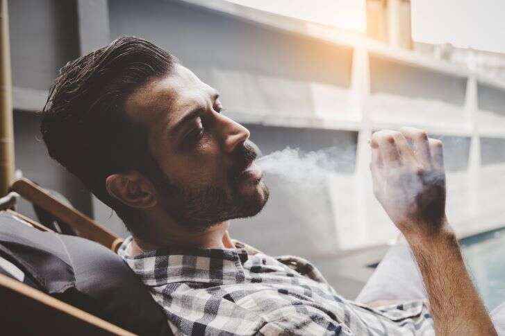 Mann sitzt in einem Liegestuhl und raucht Cannabis.