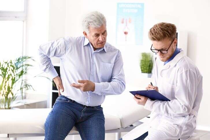 Älterer Mann zeigt einem Arzt in seiner Praxis den schmerzenden Bereich an seinem Oberkörper.