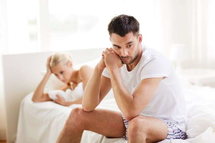 Mann sitzt mit nachdenklichem Blick auf einem Bett, hinter ihm liegt eine Frau und blickt enttäuscht auf den Boden.