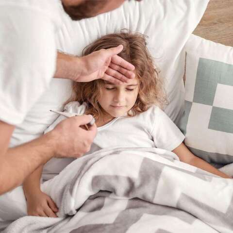 Mann misst mit einem Fieberthermometer die Temperatur eines Mädchens, die in ihrem Bett liegt.